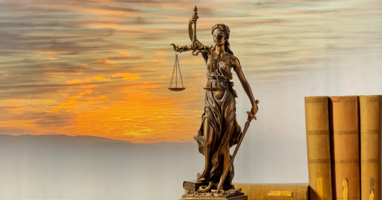 eine Statue der Justitia, auch bekannt als Themis, vor der Kulisse eines lebhaften Sonnenuntergangs